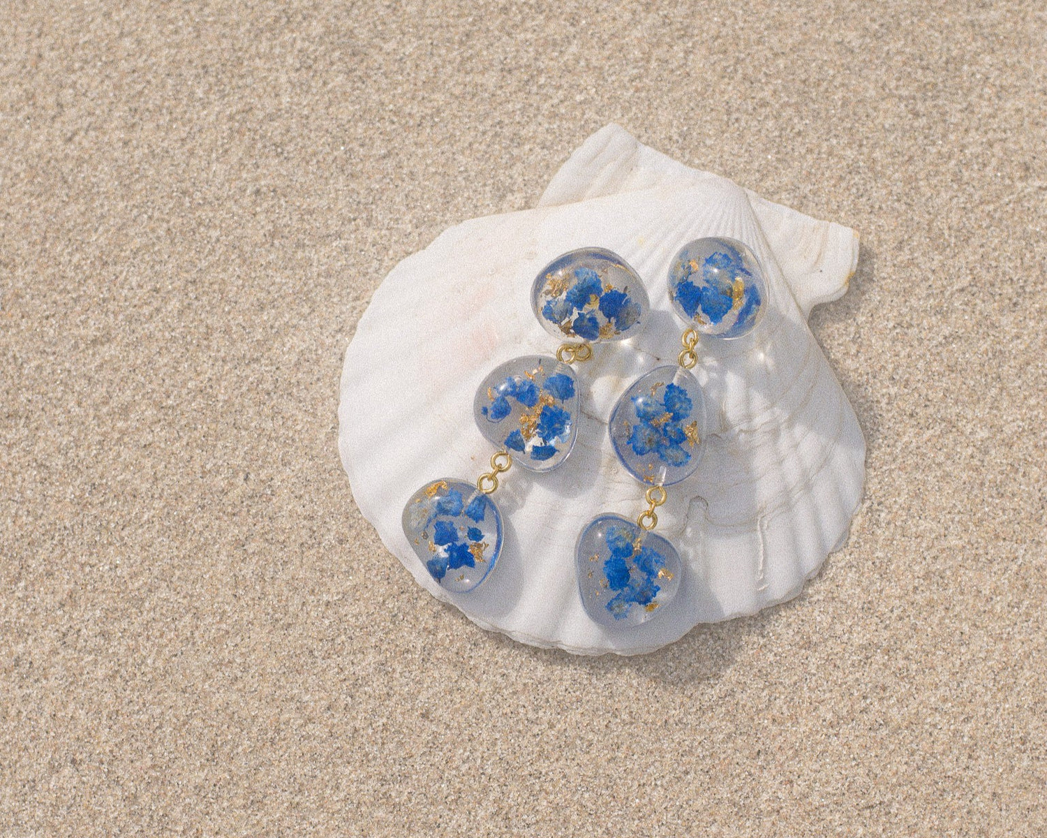 Shell with blue flower earrings on a sandy surface
