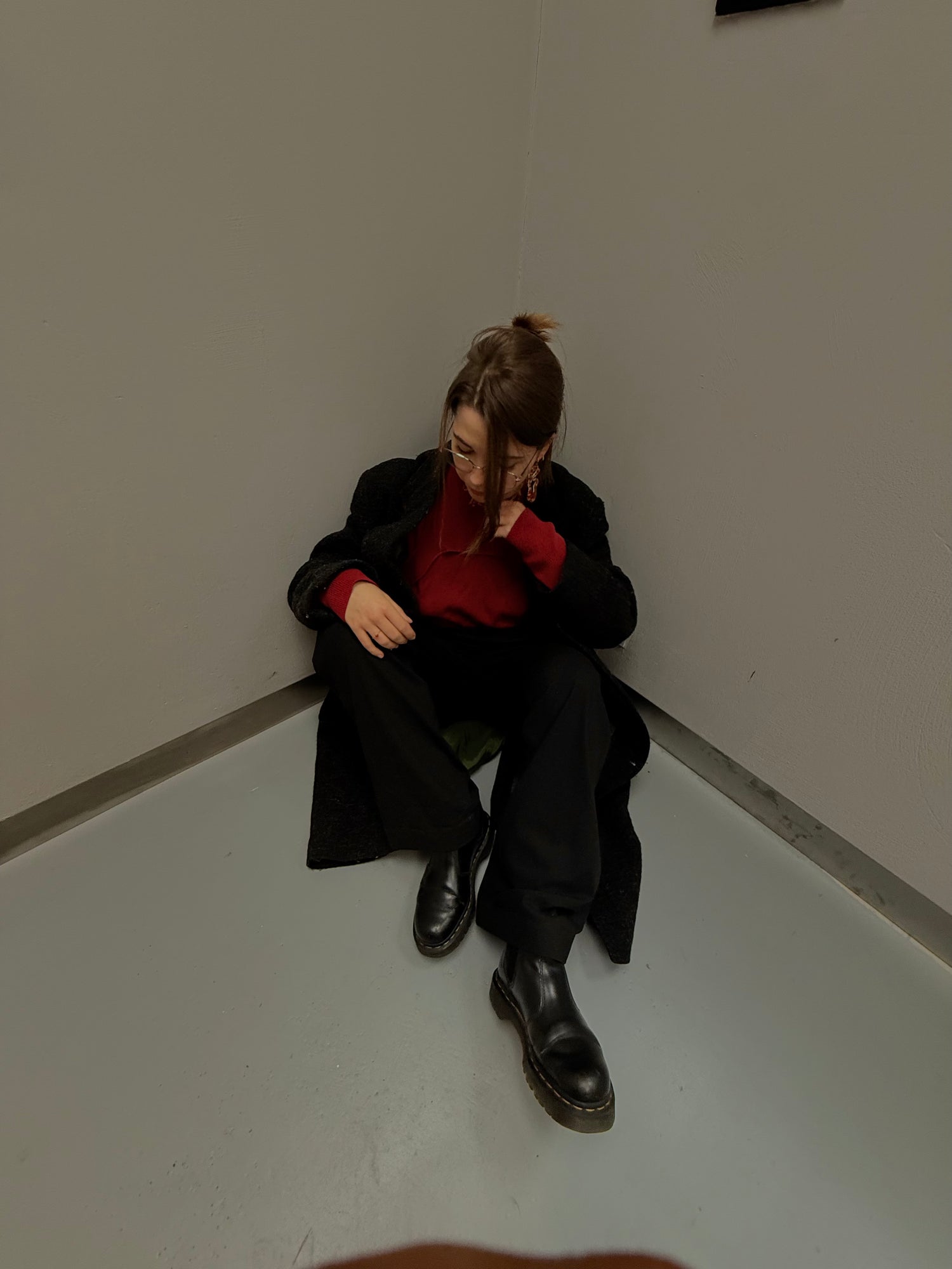 Girl sitting in a corner wearing a black and red outfit along with earrings containing real red flowers