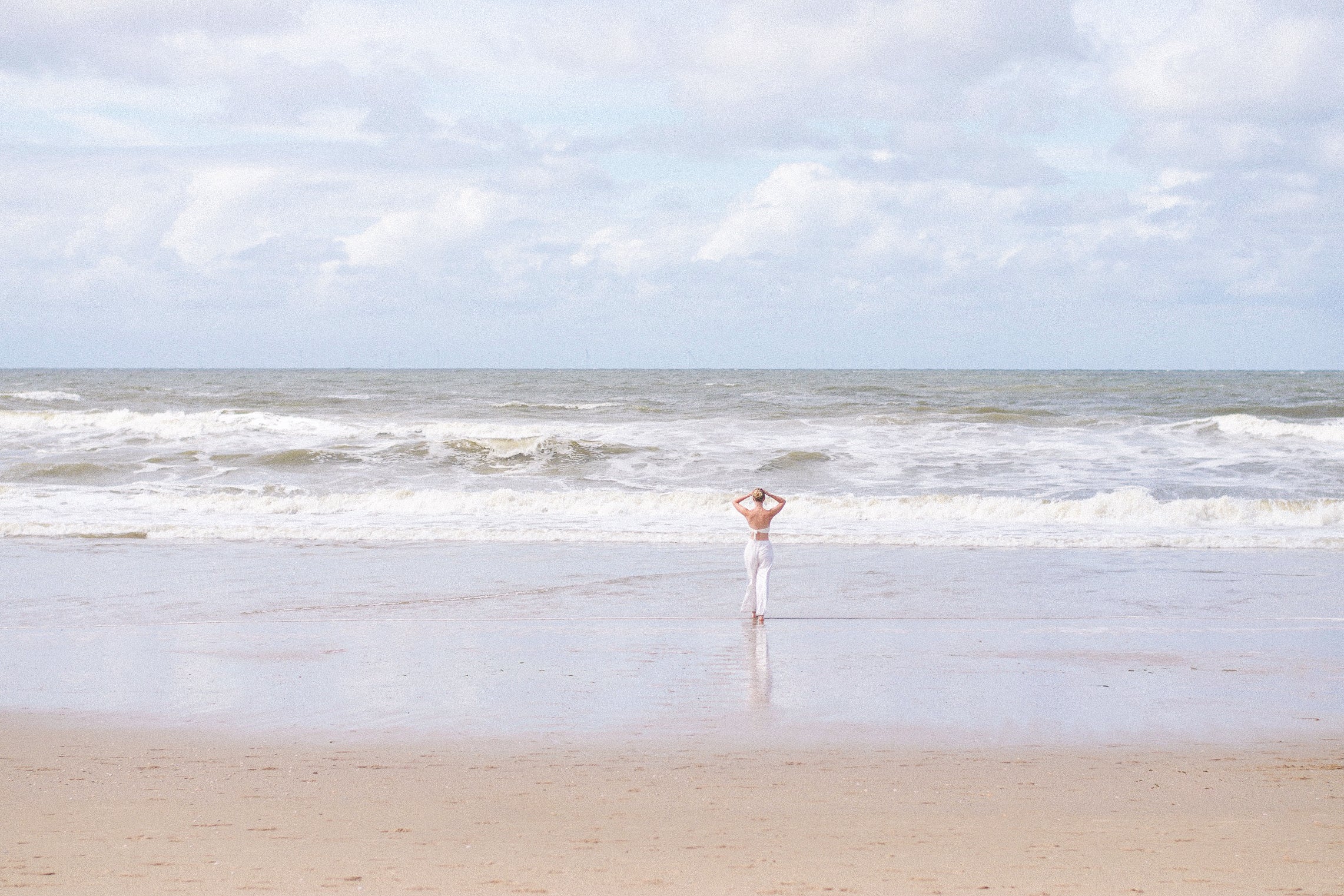 Person standing on a beach in Scheveningen with ocean waves and a clear sky