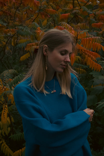 Woman in a blue sweater standing among autumn foliage