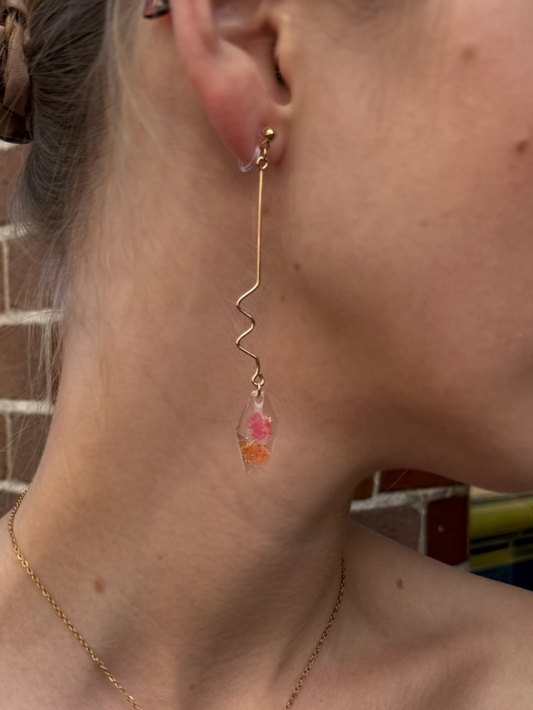 Close-up of a person wearing a necklace and earrings with a brick wall background