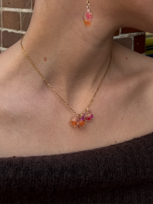 Close-up of a person wearing a necklace and earrings with a brick wall background