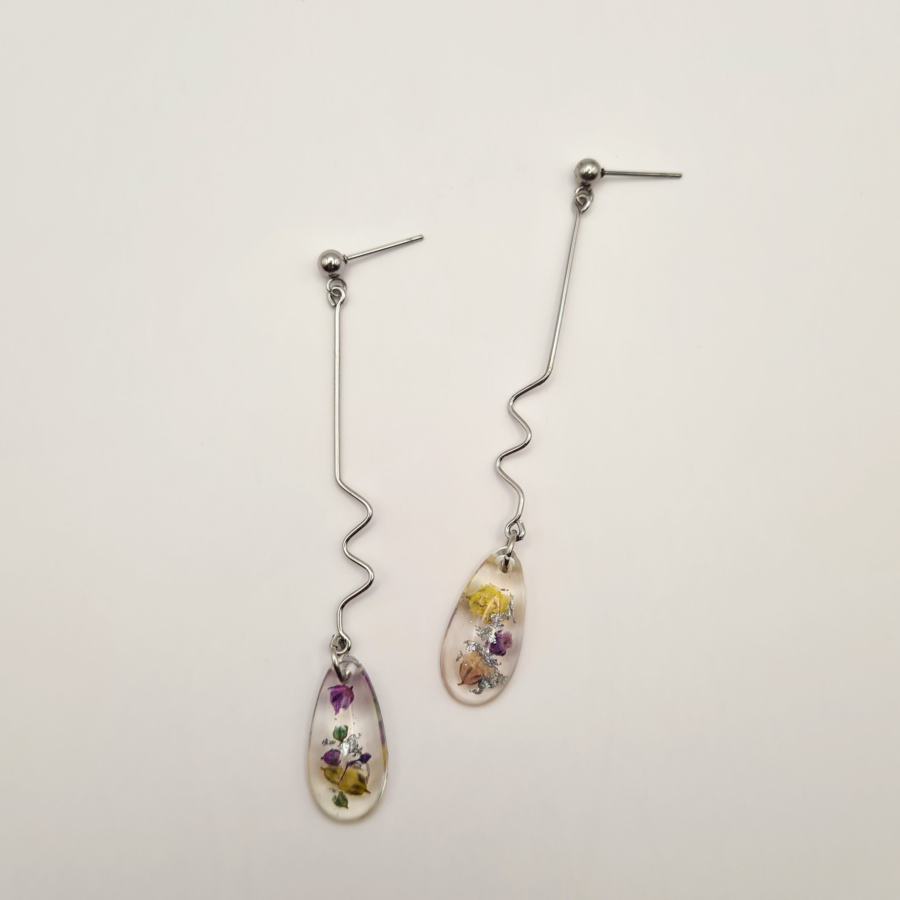 Teardrop-shaped earrings with real flowers on a light background