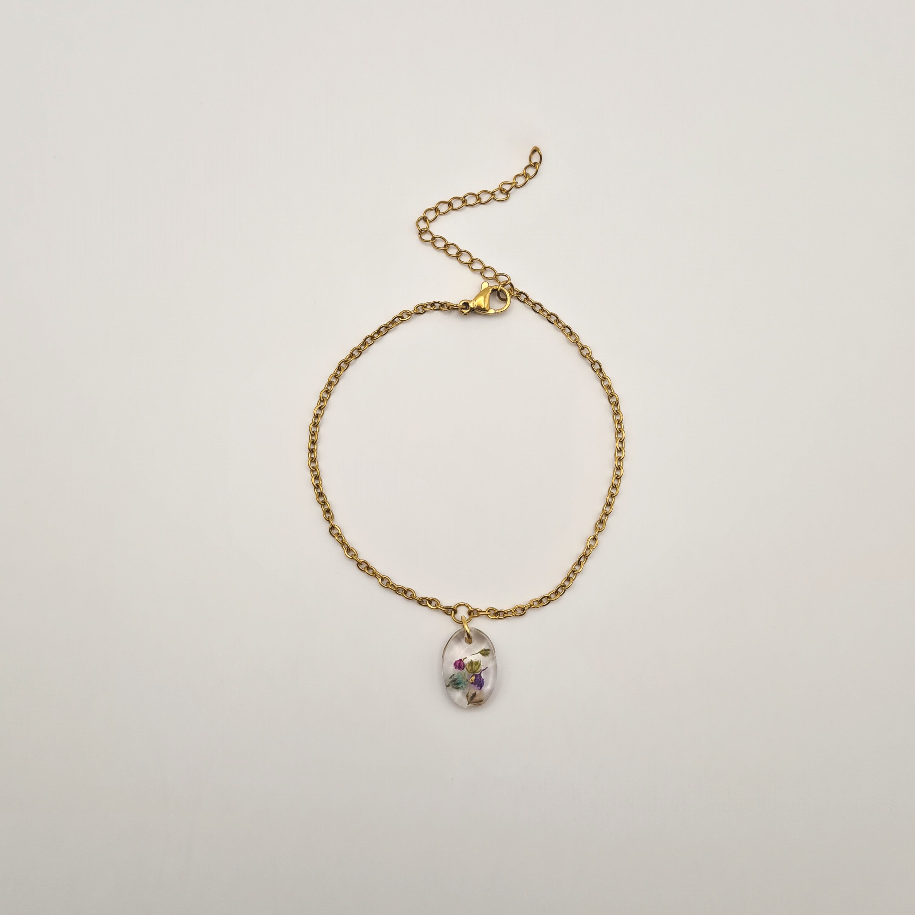 Gold bracelet with a small pendant containing real dried flowers on a light gray background