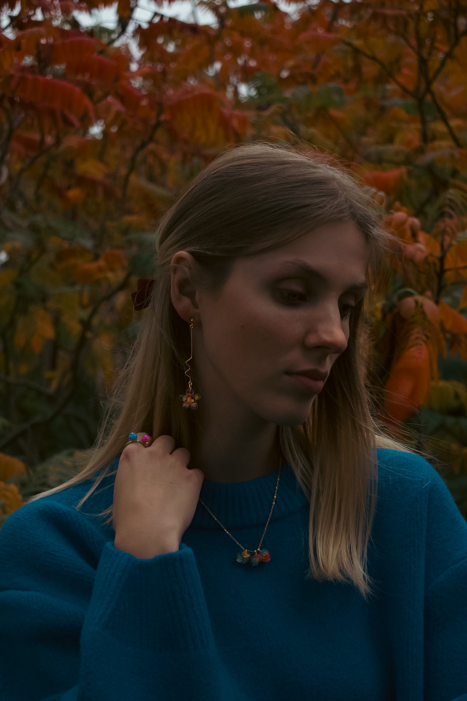 Woman adjusting her earrings with a blurred autumn background