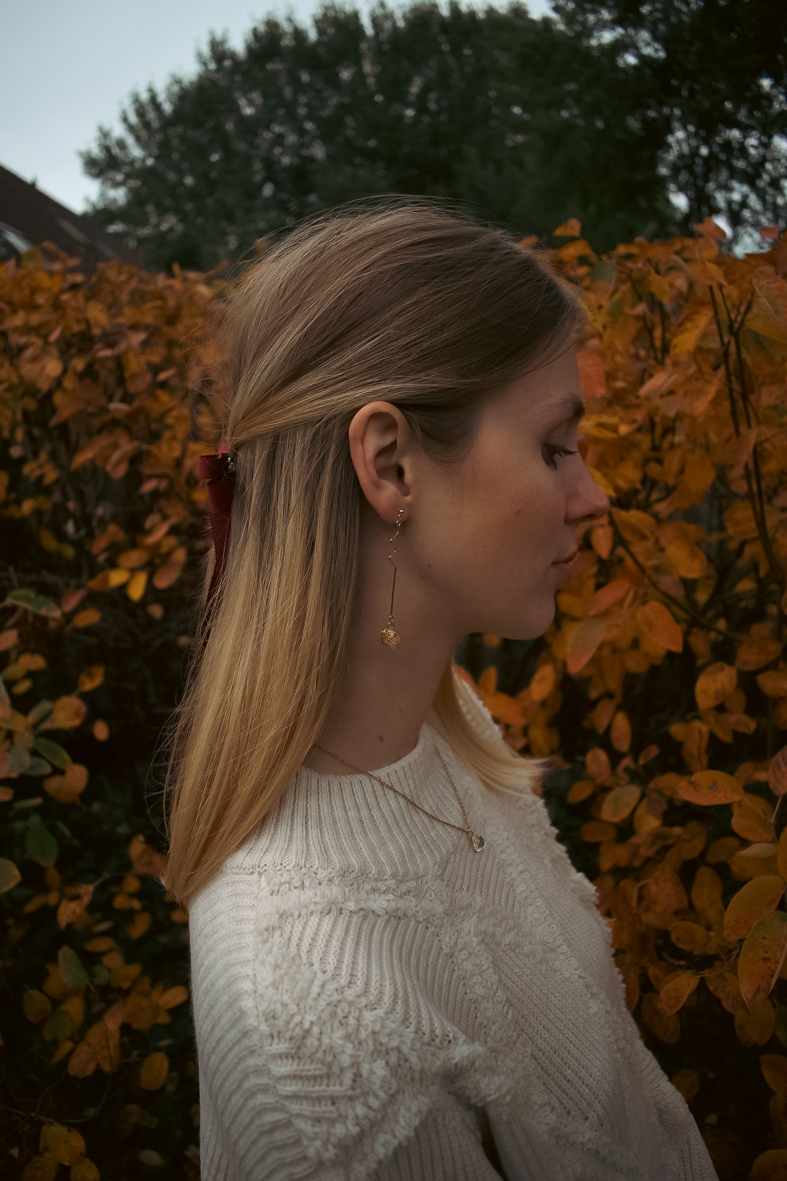Woman wearing a white sweater with autumn foliage in the background