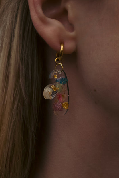 Close-up of an ear wearing a colorful teardrop earring with a blurred background