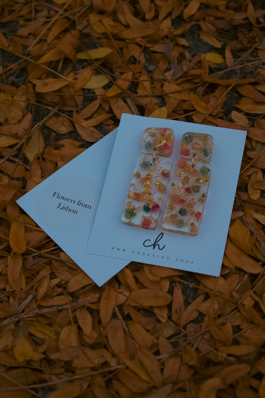Decorative earrings on a card with 'Flowers from Lisbon' text, placed on orange leaves.