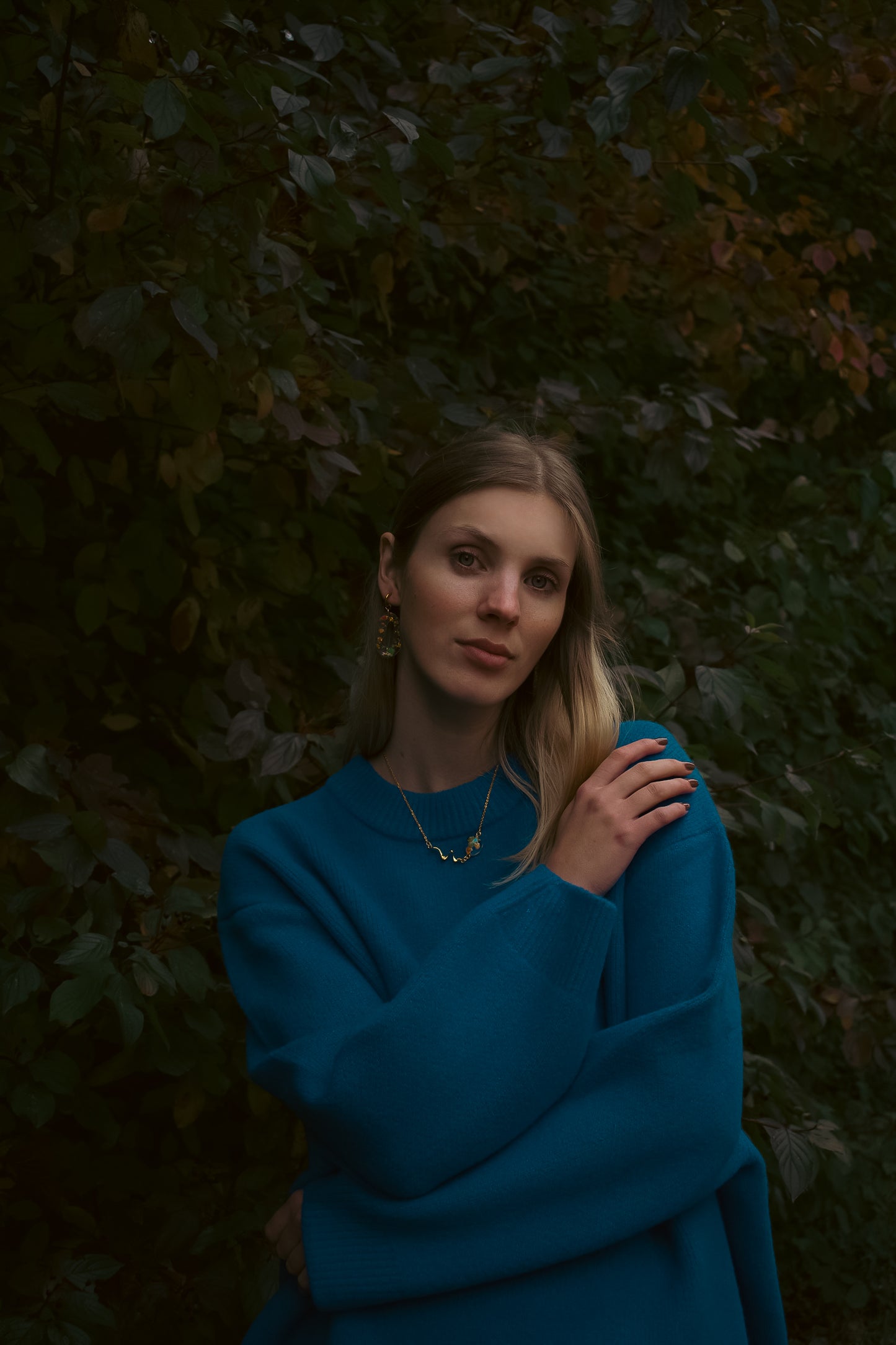 Woman in a blue dress standing against a dark, leafy background
