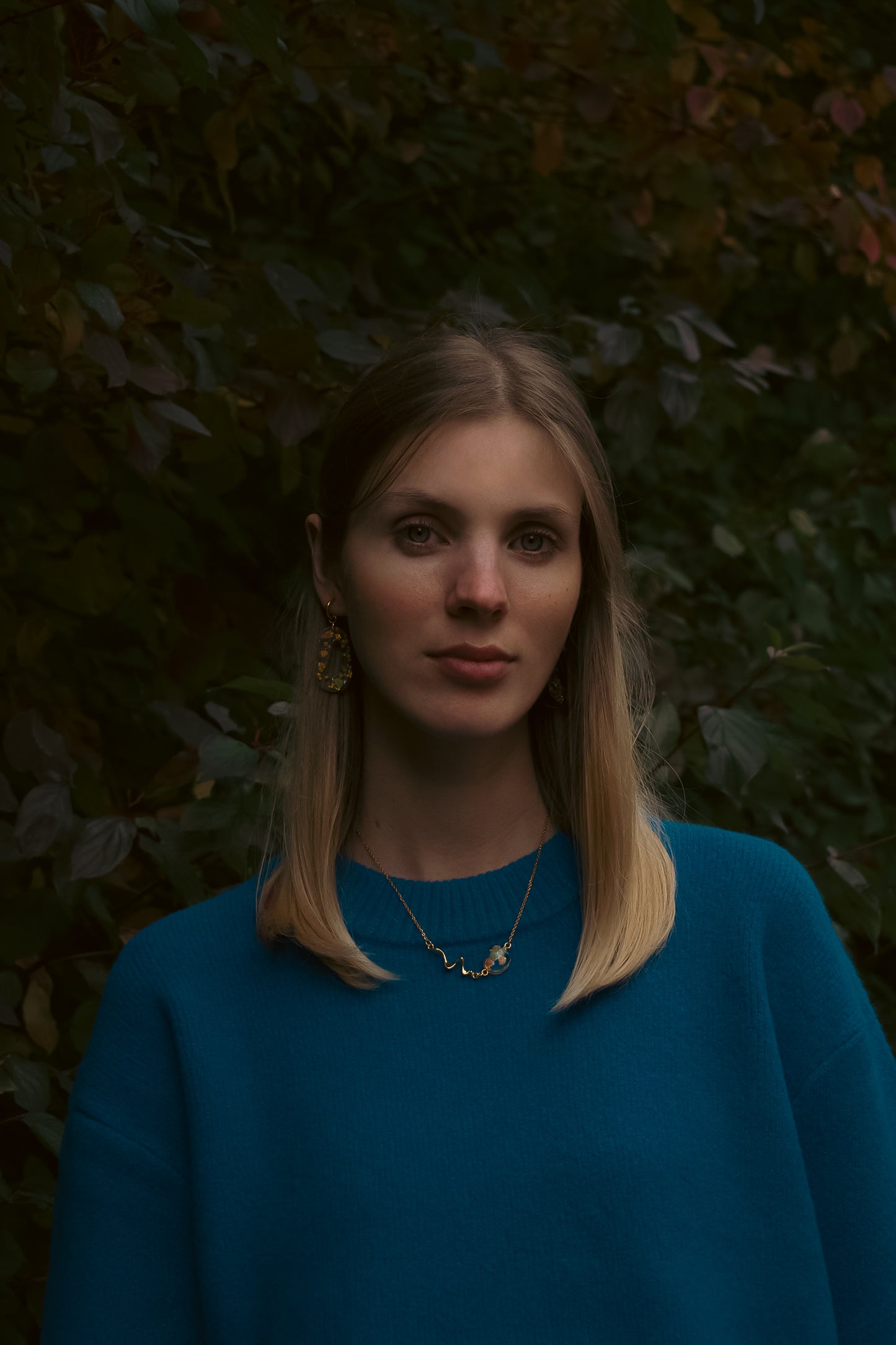 Woman wearing a blue sweater against a dark leafy background
