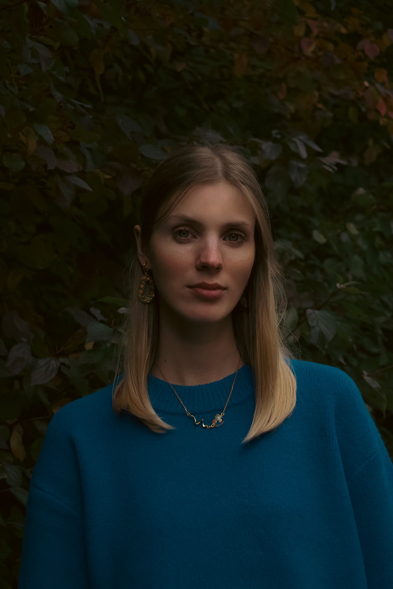 Woman wearing a blue sweater against a dark leafy background