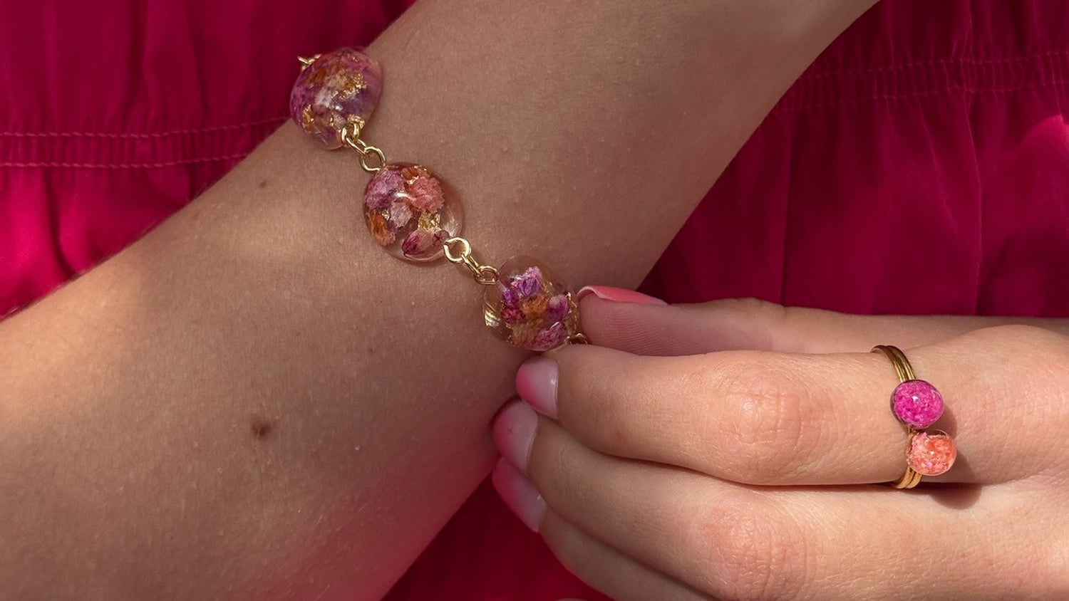 Close-up of a wrist wearing a floral bracelet with a matching ring against a red background.