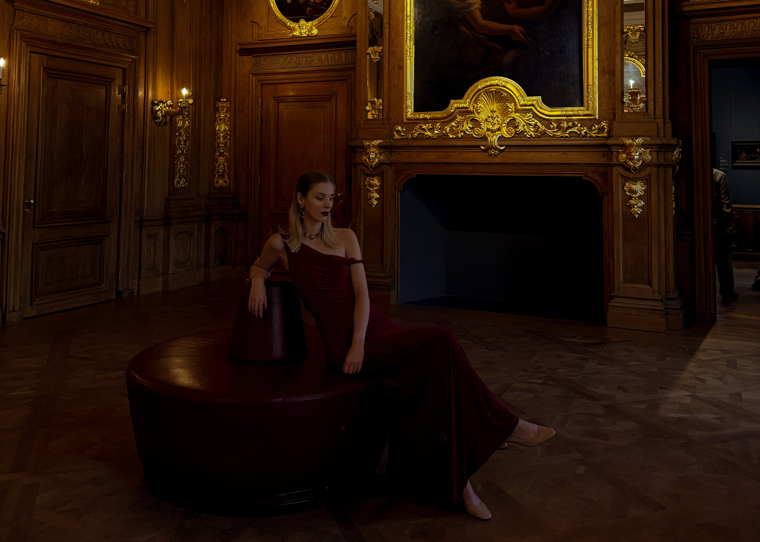 Woman in a red dress sitting in an ornate room with a chandelier and paintings.