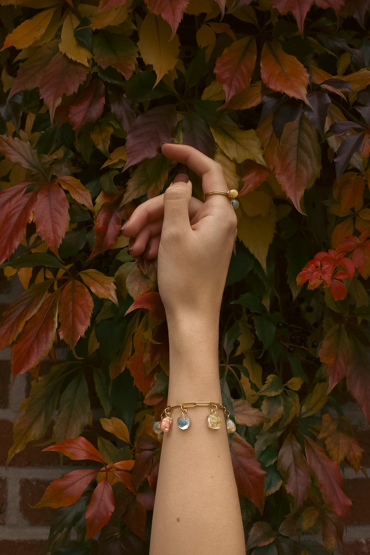 Hand on autumn leaves wearing a charm bracelet with pendants containing real flowers