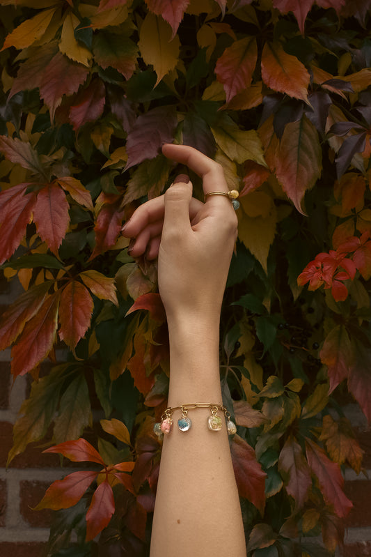 Hand on autumn leaves wearing a charm bracelet with pendants containing real flowers