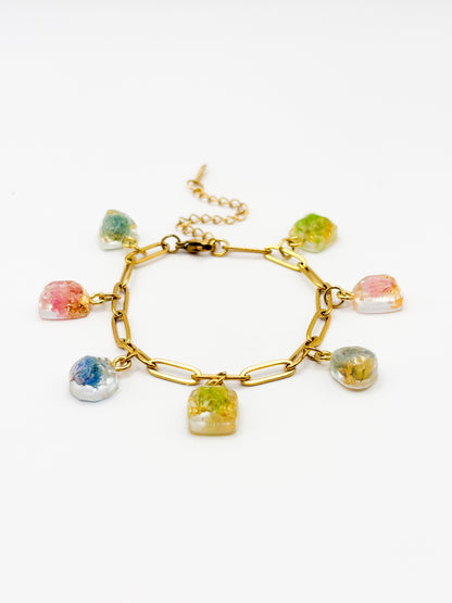 Gold bracelet with colorful gemstone charms containing real flowers on a white background