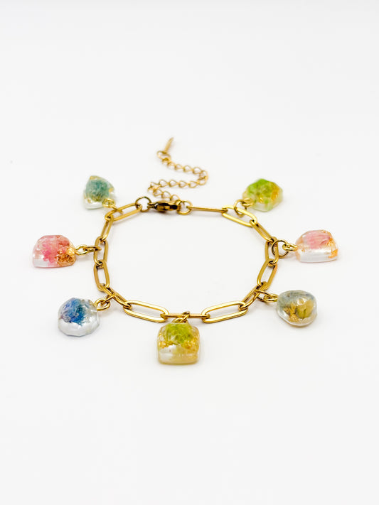 Gold bracelet with colorful gemstone charms containing real flowers on a white background