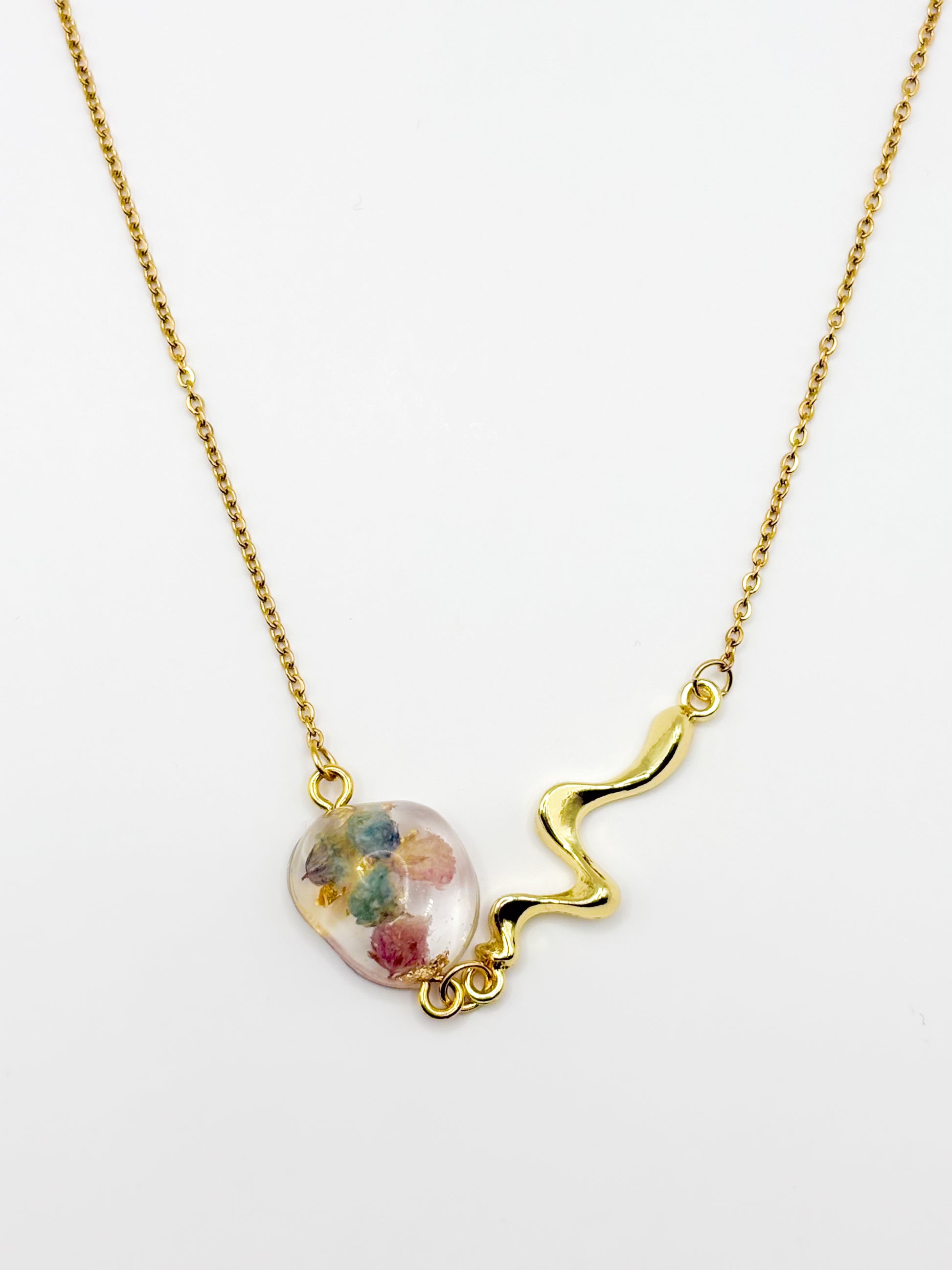 Gold necklace with a colorful bead with real flowers on a white background