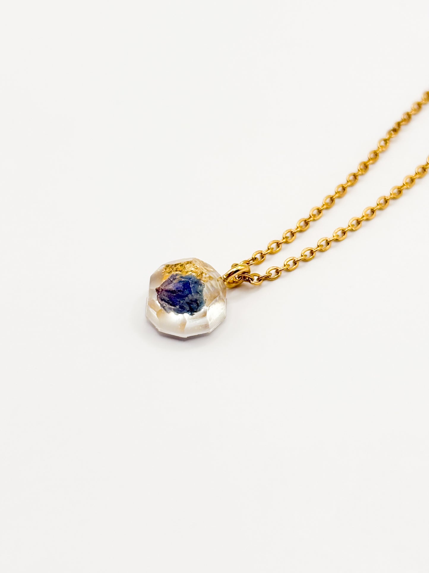 Gold necklace with a pendant featuring a blue gemstone on a white background