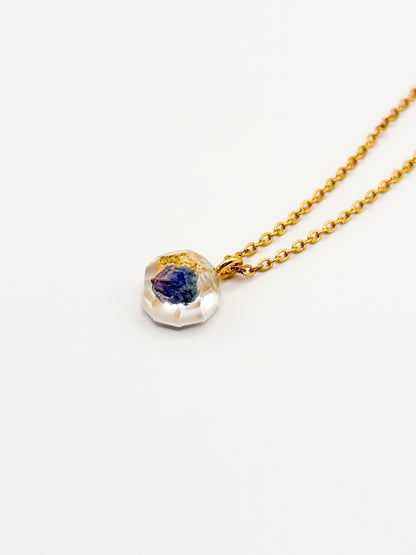 Gold necklace with a pendant featuring a blue gemstone on a white background