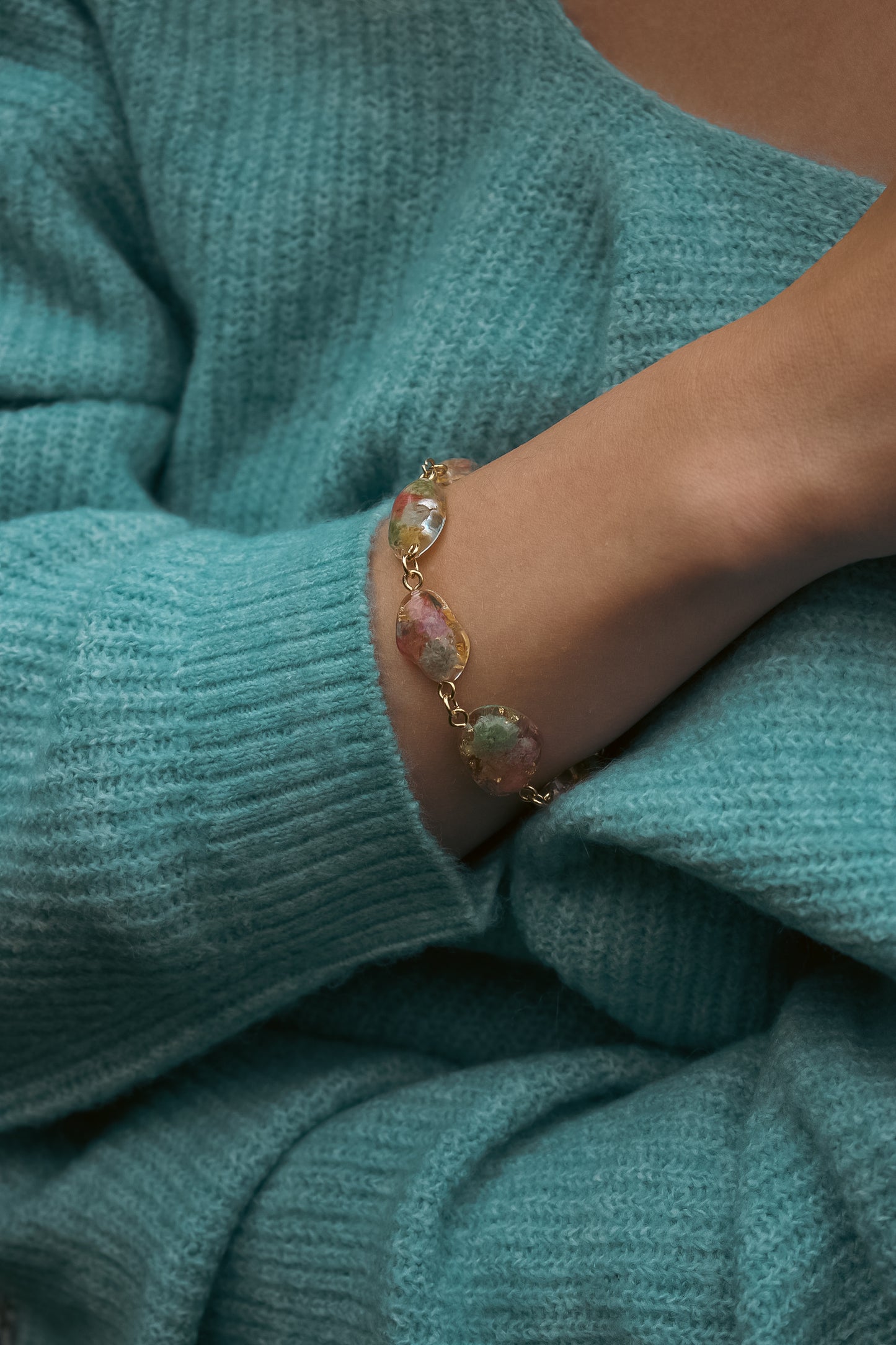 Bracelet with pendants containing real flowers on a teal sweater