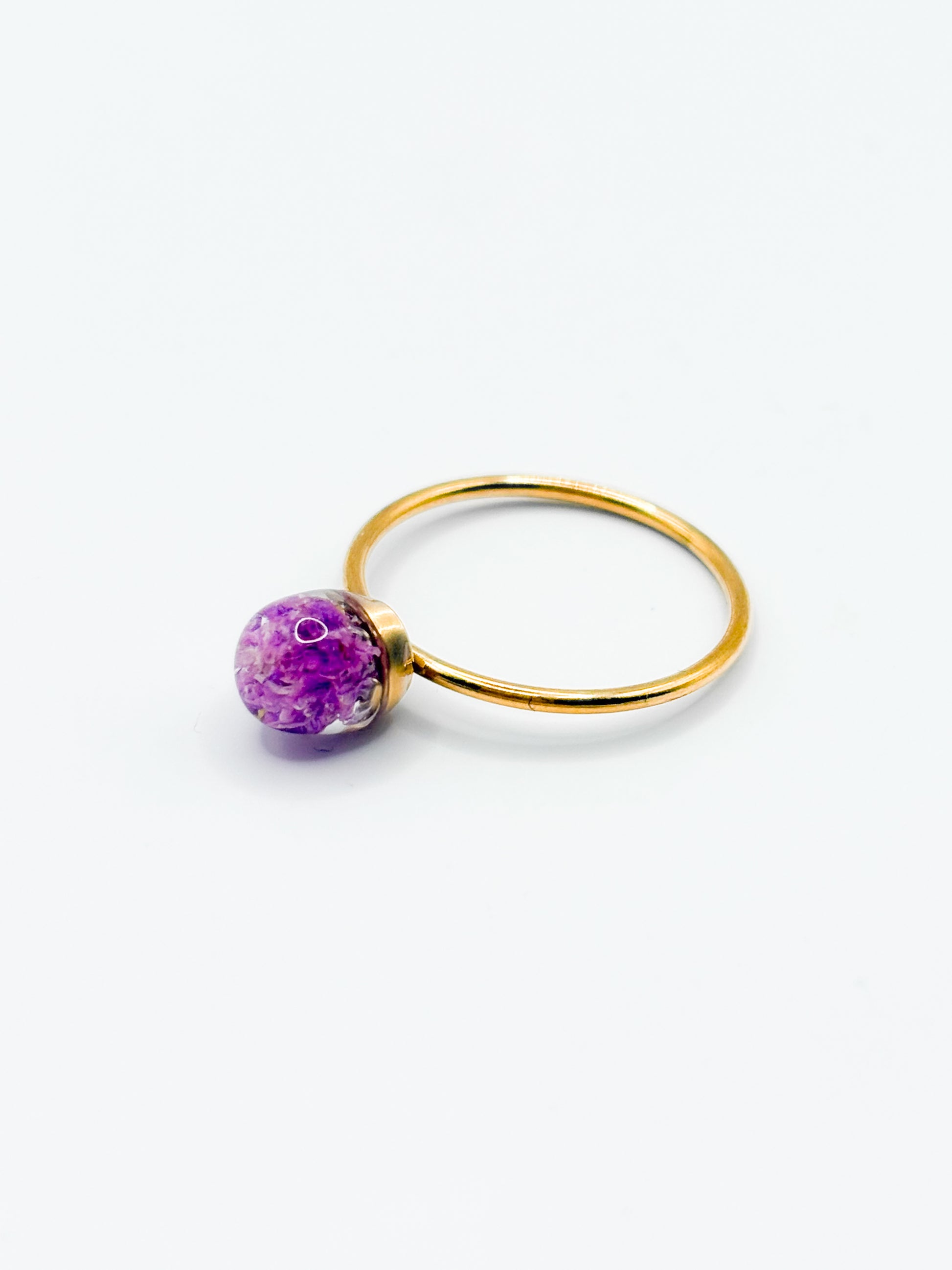 Gold ring with a purple flower gemstone on a white background